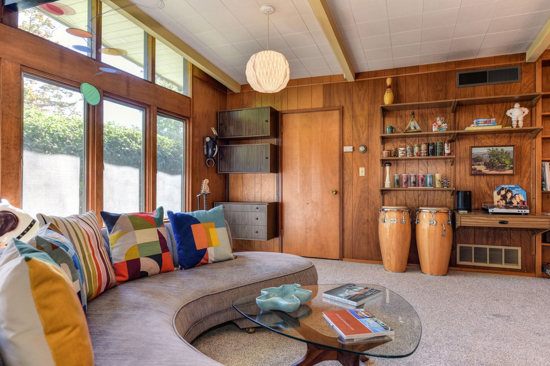 Salon mid-century modern z drewnianą boazerią i kolorowymi poduszkami